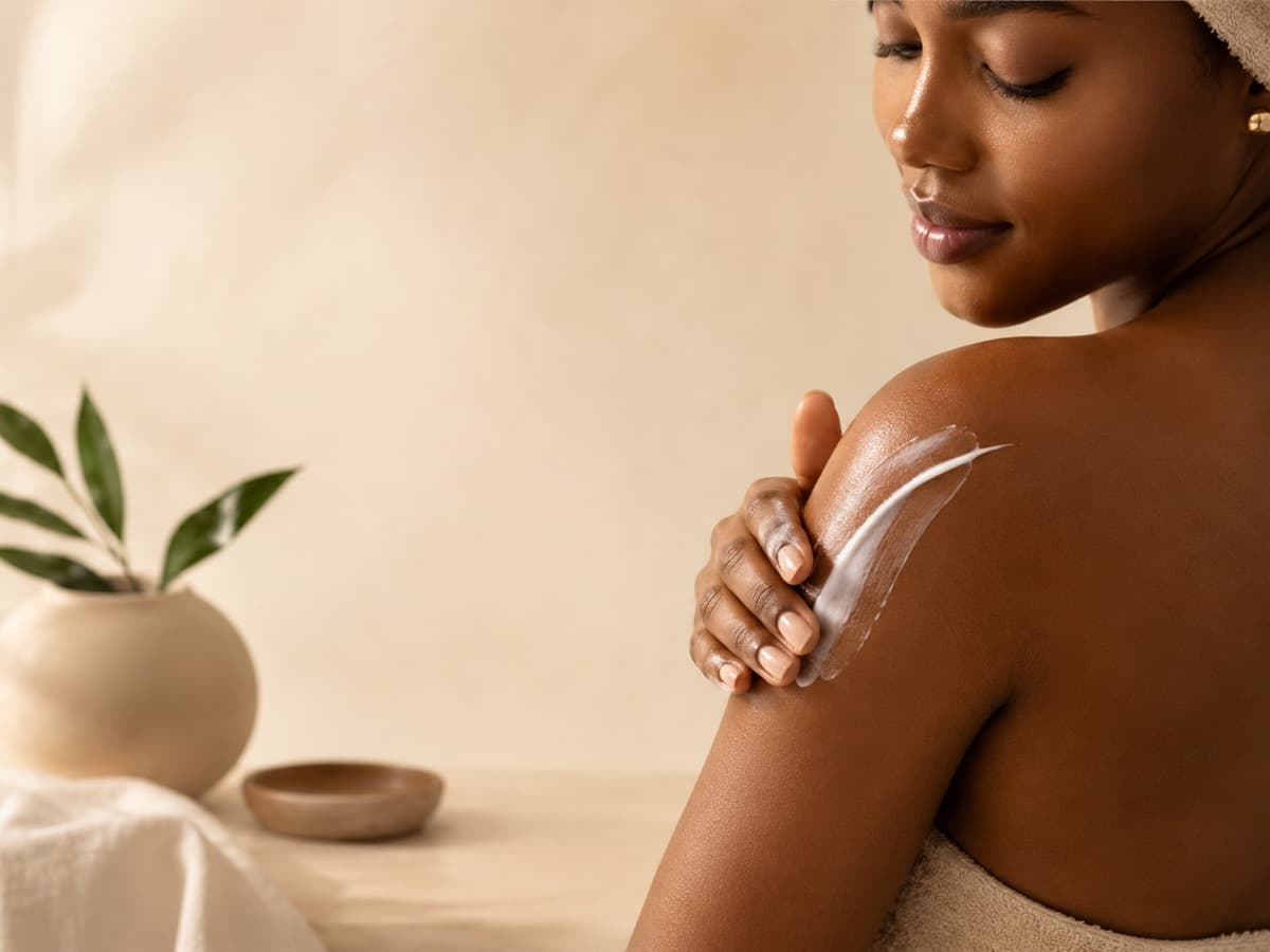 Femme noire appliquant une crème hydratante sur son épaule